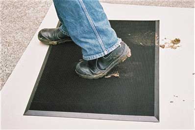 A person wiping dirty boots onto a black Multigard 220 mat