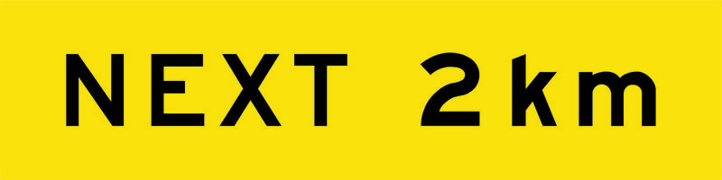 A yellow and black Next 2km Sign