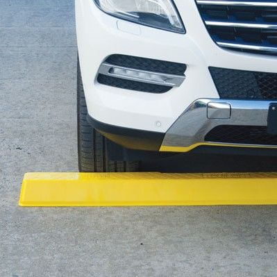 A yellow Plastic Wheel Stop under the front of a white car