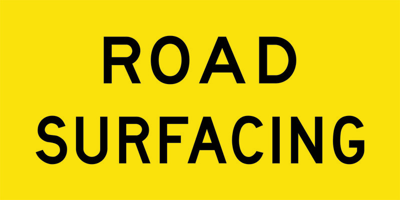 A yellow and black Road Surfacing Sign